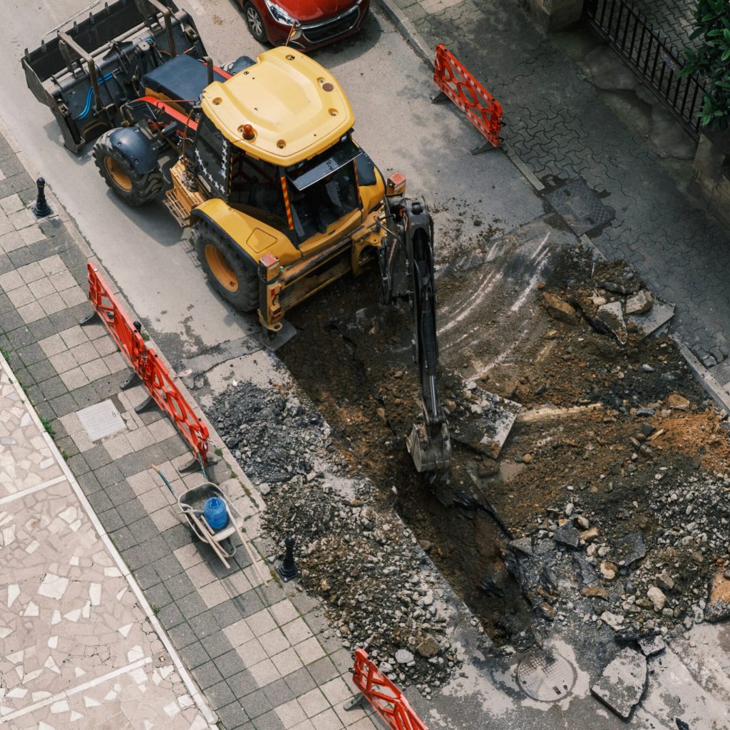 An excavator repairs sewer storm hatches ata street on a summer