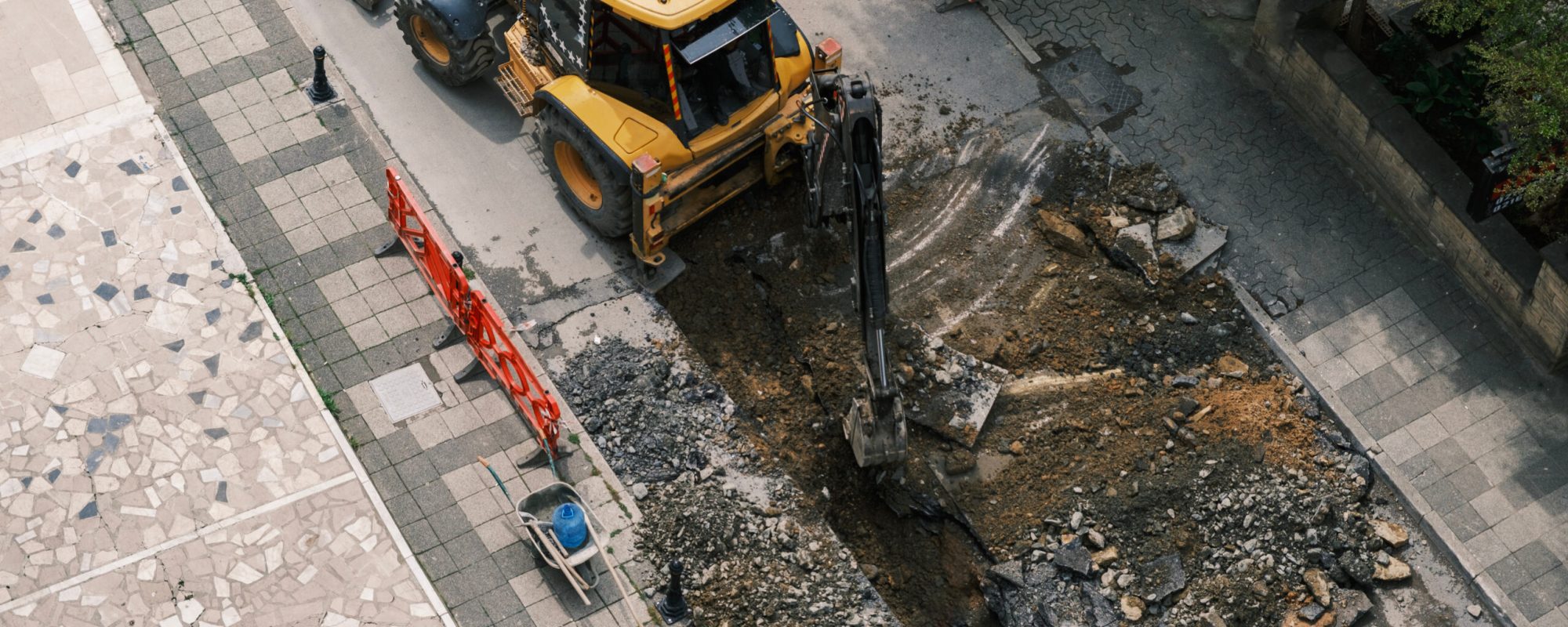 An excavator repairs sewer storm hatches ata street on a summer